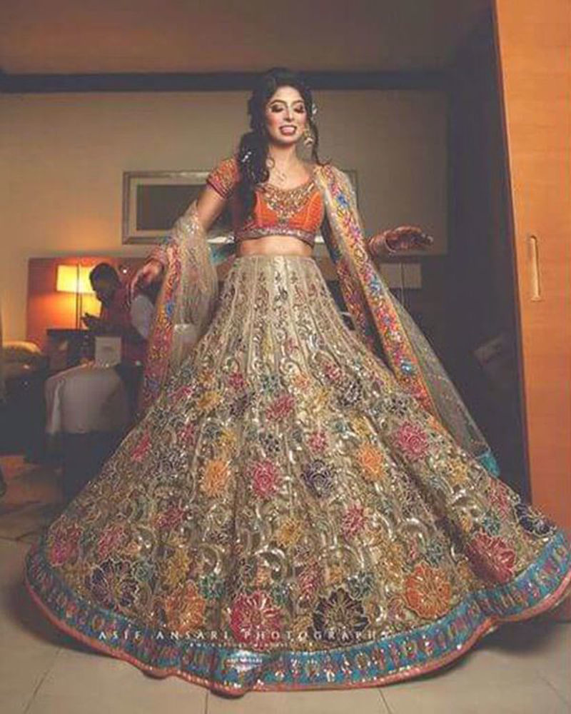 Picture of Sudha Hemani makes a beautiful bride in our floral embellished lehnga, paired with a bright orange choli and intricately bordered dupatta for her mehndi